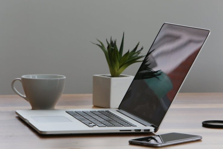 mesa de escritório com notebook, caneca, celular e um pequeno vaso